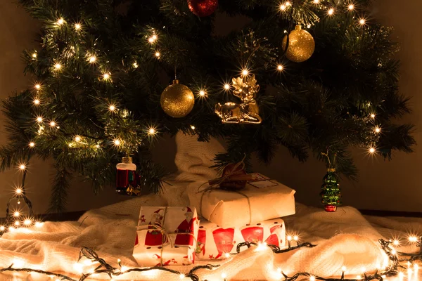 Χριστουγεννιάτικα δώρα κάτω από gerlyandoy διακοσμημένα, φωτεινά κίτρινα και κόκκινα μπαλάκια χριστουγεννιάτικο δέντρο — Φωτογραφία Αρχείου