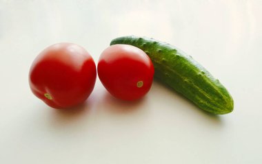 Turuncu domatesli fotoğraf ve beyaz bir masada yeşil salatalık. Sebze mahsulü.