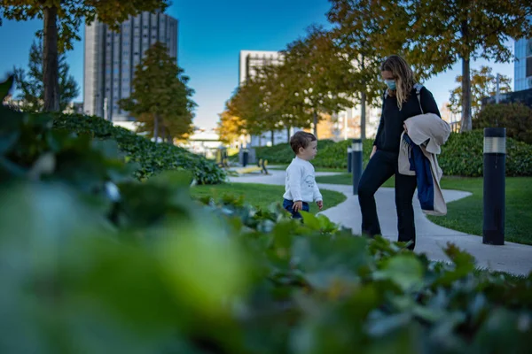 Anne ve oğlu mavi gökyüzü olan bir parkta konuşuyor.