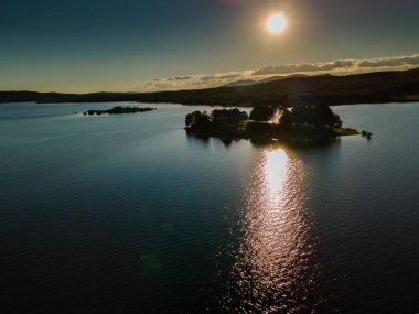 Gölde gün batımı bir ada ve suda güneşin yansımaları.
