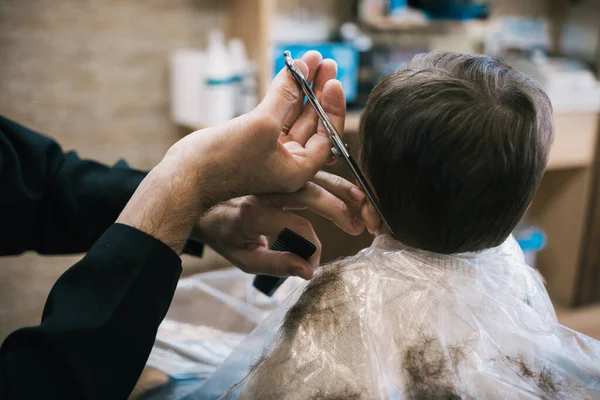 Bir kuaförde bir bebek ve çocuğun saçını makas ve tarakla kesen tanınmamış bir adam.