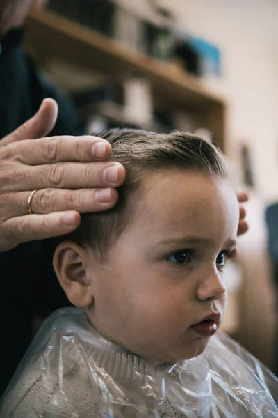 Bir kuaförde bir bebek ve çocuğun saçını makas ve tarakla kesen tanınmamış bir adam.