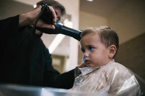 Bir kuaförde bir bebek ve çocuğun saçını makas ve tarakla kesen tanınmamış bir adam.