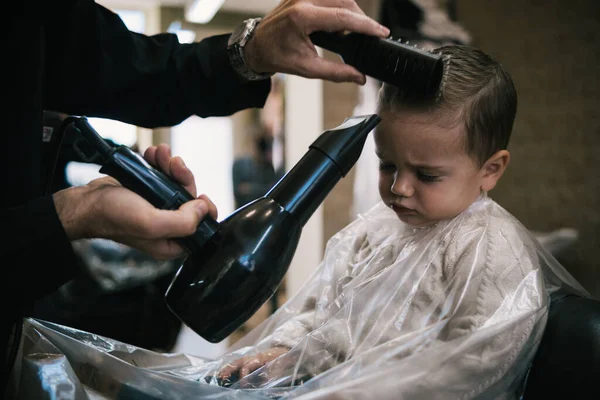 Bir kuaförde bir bebek ve çocuğun saçını makas ve tarakla kesen tanınmamış bir adam.