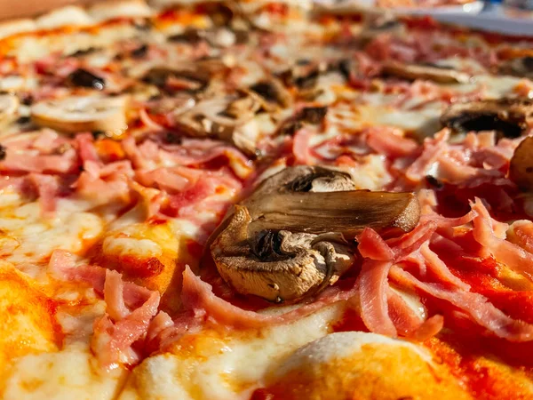 Ön planda taze mantar, peynir ve jambonlu pizza var.