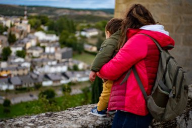 Kırmızı at kuyruklu ve paltolu sarışın kadın kahverengi ceketli sarışın bebeğiyle kendine bakıyor.