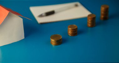Coins, sheet of paper and pen, paper house on surface of blue. Selective focus