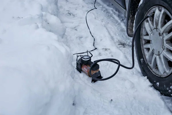 Электронасос с монометром накачивает воздух в колесо автомобиля в зимний день — стоковое фото