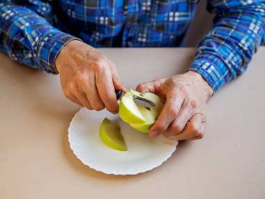 Adam elmayı bıçakla keser. Elma dilimi beyaz tabakta duruyor.