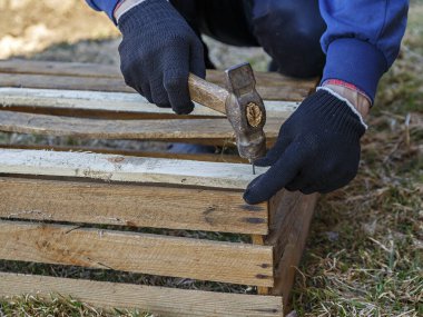 Kahverengi tahtalardan yapılmış tahta kutu, siyah eldivenli adam çekiçle tahtaya çivi çakıyor..