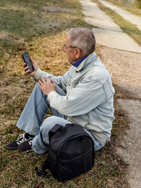 Elderly Man Denim Jacket Sits Side Road Looks His Smartphone — Stock Photo, Image