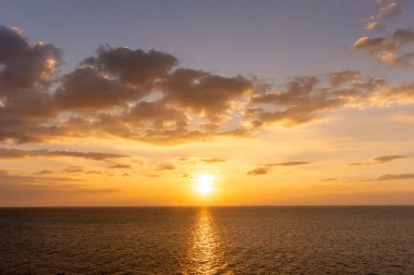 Günbatımının yansıması okyanus. Bulutların ardında güzel bir gün batımı ve okyanus manzarasının üstünde mavi bir gökyüzü.