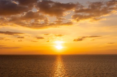 Günbatımının yansıması okyanus. Bulutların ardında güzel bir gün batımı ve okyanus manzarasının üstünde mavi bir gökyüzü.