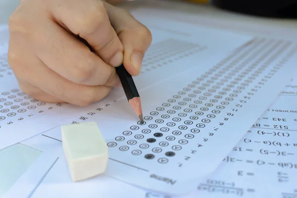 Students hand holding pencil writing selected choice on answer sheets and Mathematics question sheets. students testing doing examination. school exam
