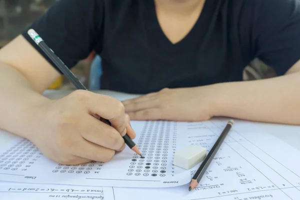 Woman students hand holding pencil writing selected choice on answer sheets and Mathematics question sheets. students testing doing examination. school exam