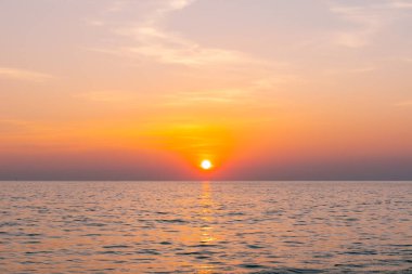 Gün batımı yansıma denizi. Bulutların ardında güzel bir gün batımı ve deniz manzarasının üstünde mavi bir gökyüzü.