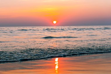 Gün batımı yansıma denizi. Bulutların ardında güzel bir gün batımı ve deniz manzarasının üstünde mavi bir gökyüzü.