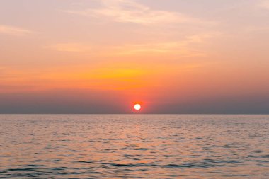 Gün batımı yansıma denizi. Bulutların ardında güzel bir gün batımı ve deniz manzarasının üstünde mavi bir gökyüzü.