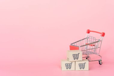 Alışveriş konsepti: pembe arka planda kırmızı alışveriş arabasında karton kutular veya karton kutular. Çevrimiçi alışveriş tüketicileri evden ve teslimat servisinden alışveriş yapabilirler. kopyalama alanı ile