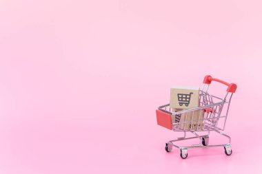 Alışveriş konsepti: pembe arka planda kırmızı alışveriş arabasında karton kutular veya karton kutular. Çevrimiçi alışveriş tüketicileri evden ve teslimat servisinden alışveriş yapabilirler. kopyalama alanı ile