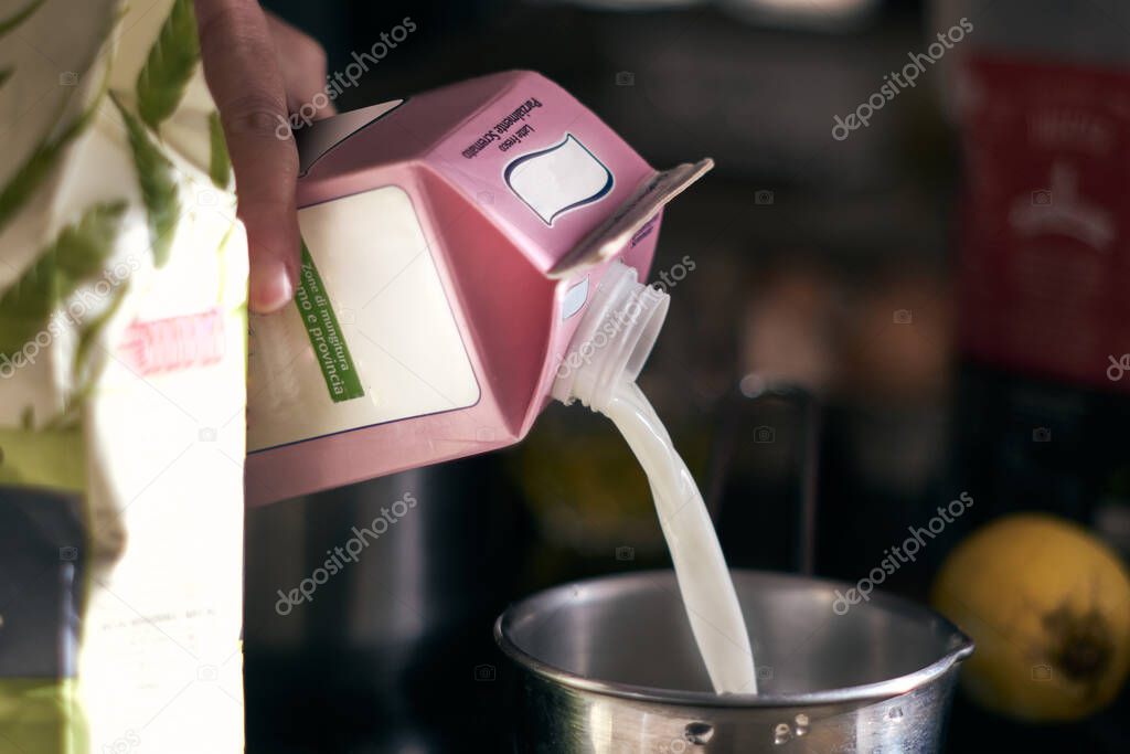Hand pours some milk into a bowl. close up cropped photo, blurred background.