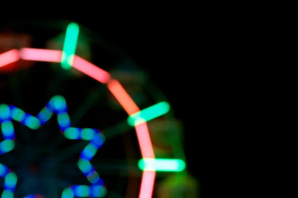 Размытое изображение колеса обозрения в парке аттракционов ночью — стоковое фото