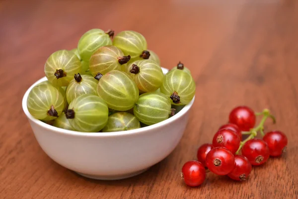 Gooseberry dan red currant di piring putih di atas meja kayu . — Stok Foto