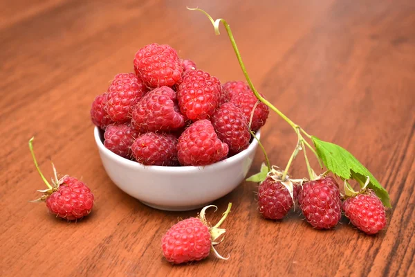 Raspberries in white plate on a wooden table, raspberry branch. Raspberrie on the table. Natural texture. — Stock Photo, Image