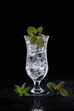 Kokteyl bardağında naneli kokteyl, sisli yüzeyinde buz ve siyah bir arka plan. Naneli yapraklar camın yanında ve camda akıyor. Taze maden suyu, buz ve iki çeşit nane ile ferahlatıcı içecek, yeşil ve yeşil-kırmızı. Alçak bir tonda.