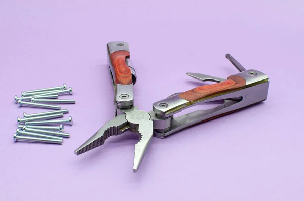 Drewniane multitool zamienione w szczypce, nóż, śrubokręt na fioletowym tle, śruby. naprawiam. naprawić — Zdjęcie stockowe