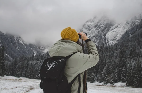 Vrouw met rugzak kijken door verrekijker, winter mistige bergen. — Stockfoto