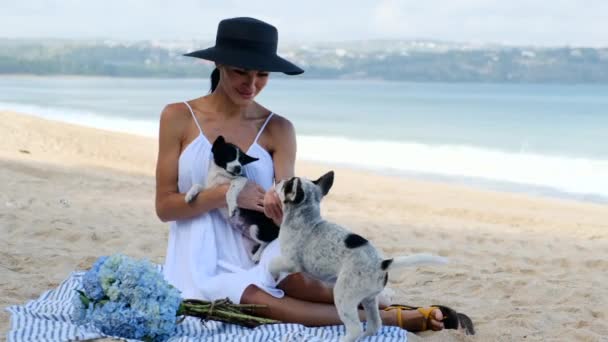 Krásná žena s květinami drží dva malé psy v pláži oceánu — Stock video