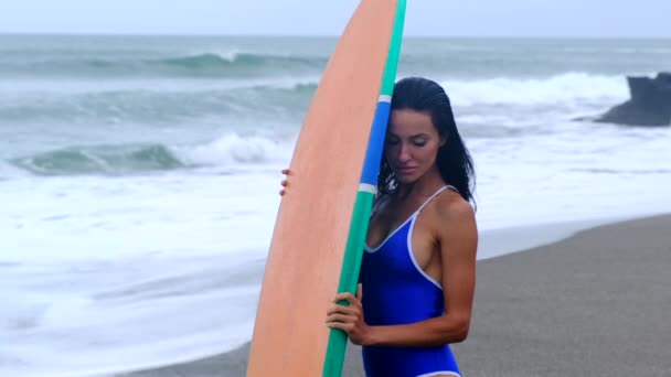 Mayo giymiş genç bir kızın okyanus kenarında sörf tahtası ile poz verişi. — Stok video