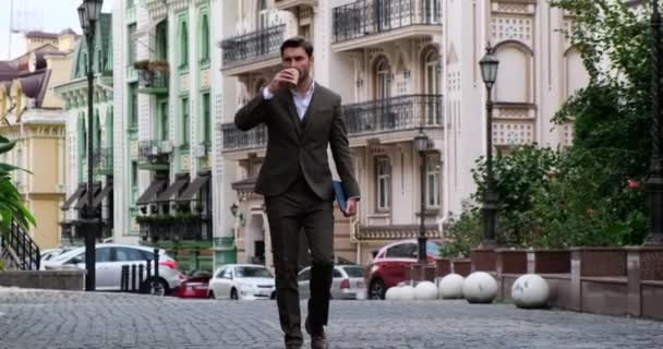 Un tânăr om de afaceri bea cafea în timp ce merge la muncă . — Videoclip de stoc