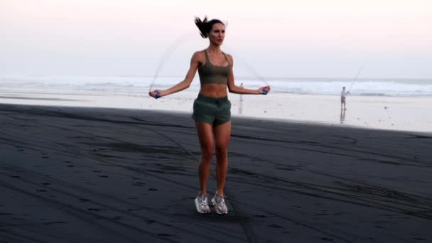 Spor kıyafetli bir kız okyanusun kenarında ip atlıyor. — Stok video