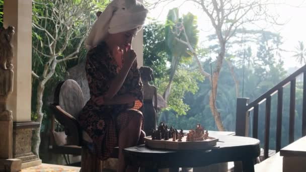 Schönes Mädchen im Bademantel spielt handgemachtes Schach in der Villa — Stockvideo