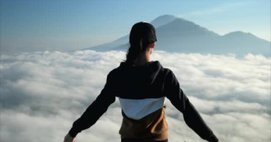 Genç bir kız bir dağın tepesinde duruyor ve ellerini havaya kaldırıyor, Bali.