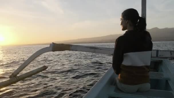 Молода жінка сидить на човні, дивлячись на зграю дельфінів, які плавають біля човна — стокове відео