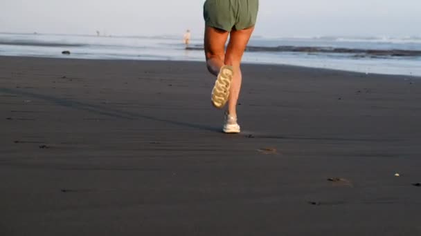Piernas deportivas en zapatillas que corren a lo largo de la playa, zapatos mojados, entrenamiento al aire libre — Vídeos de Stock