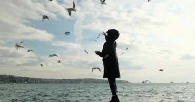 Güzel genç bir kız kışın deniz kıyısında martılara bakıyor. Yaz boyunca turizm.