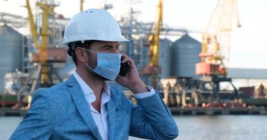 Maskeli, kasklı ve takım elbiseli bir adam telefonda konuşuyor.