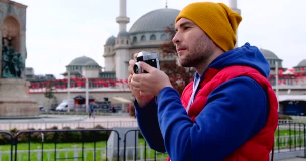 Un hombre toma una foto, mirando a la cámara, sobre el fondo de una mezquita — Vídeos de Stock