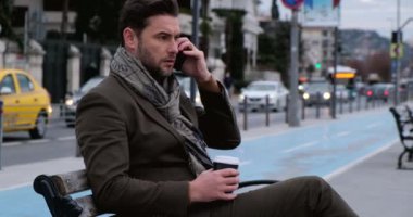 Akıllı telefon kullanan bir adam. Park Bench 'te kahveli iş adamı cep telefonu kullanıyor.