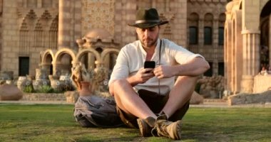 Kovboy stili yakışıklı adam çimlerin üzerinde oturuyor, telefon.mosque.egypt