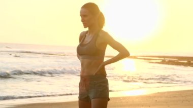 Sportif bir kadın okyanus kenarındaki plajda antrenmandan sonra dinleniyor.