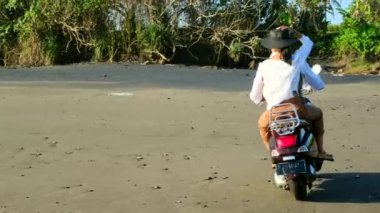 Güneş gözlüklü genç bir çift motosiklet sürerken gülümsüyor.