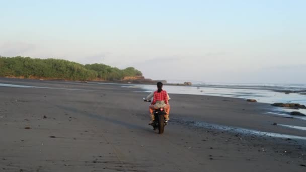 Sexy chica en pantalones cortos monta una motocicleta con un chico en la playa de la noche — Vídeo de stock