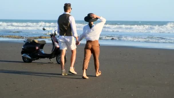 Mooi paar in liefde loopt op de oceaan kust en dansen, retro scooter — Stockvideo