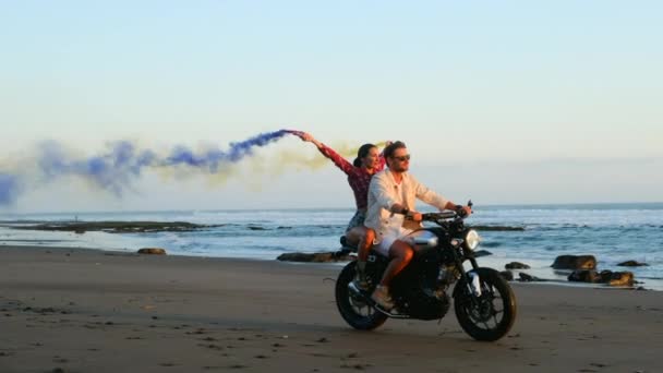 Όμορφο ζευγάρι σε ένα ρετρό μοτοποδήλατο απολαμβάνουν τη ζωή στην παραλία με χρωματιστές βόμβες — Αρχείο Βίντεο