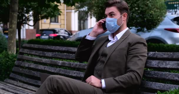 Mann im Anzug mit Maske in der Hand benutzt Handy im Park, gute Nachrichten — Stockvideo